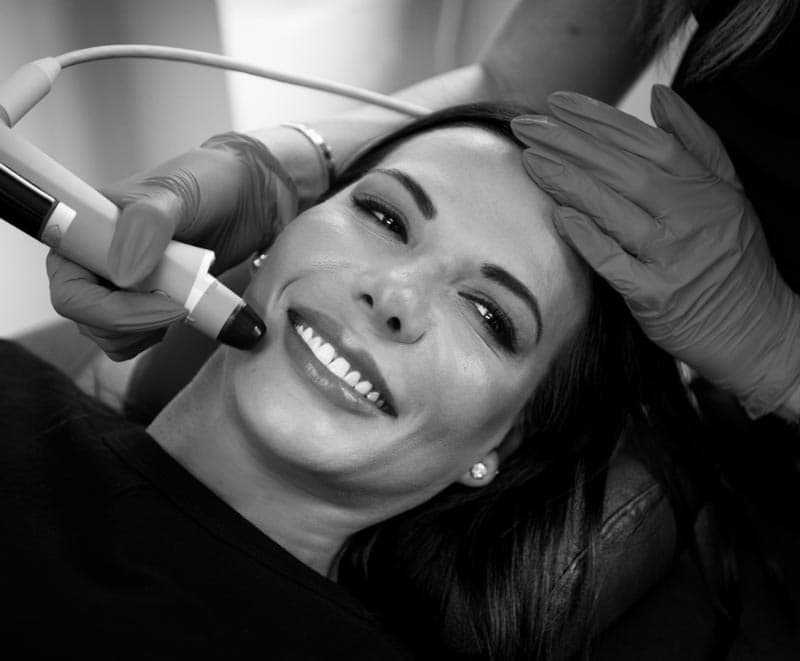 An actual patient receiving a non-invasive facial treatment, smiling comfortably while a professional uses a handheld device.