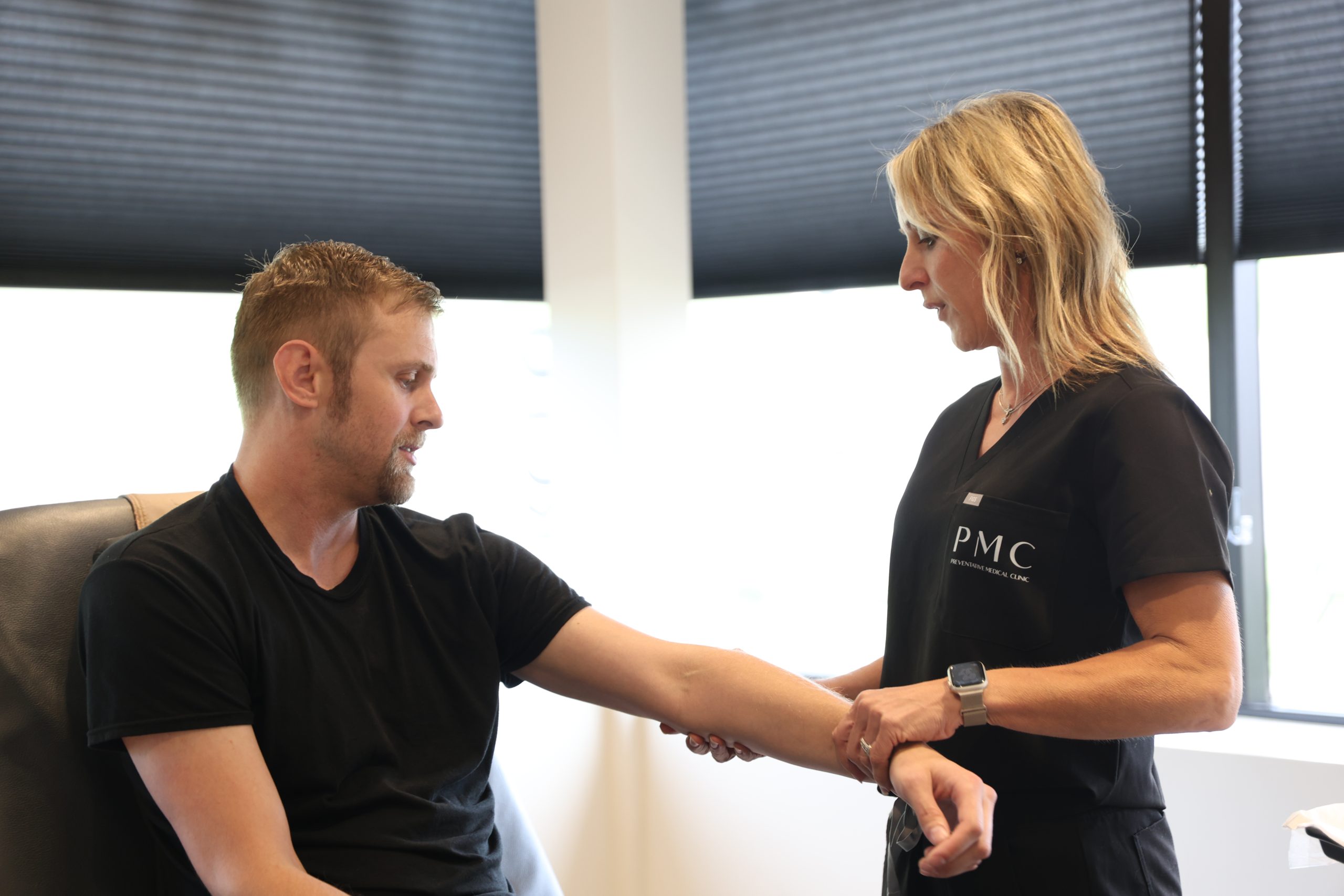 A healthcare professional examines a male patient's wrist in a clinic, discussing his condition and potential treatments.