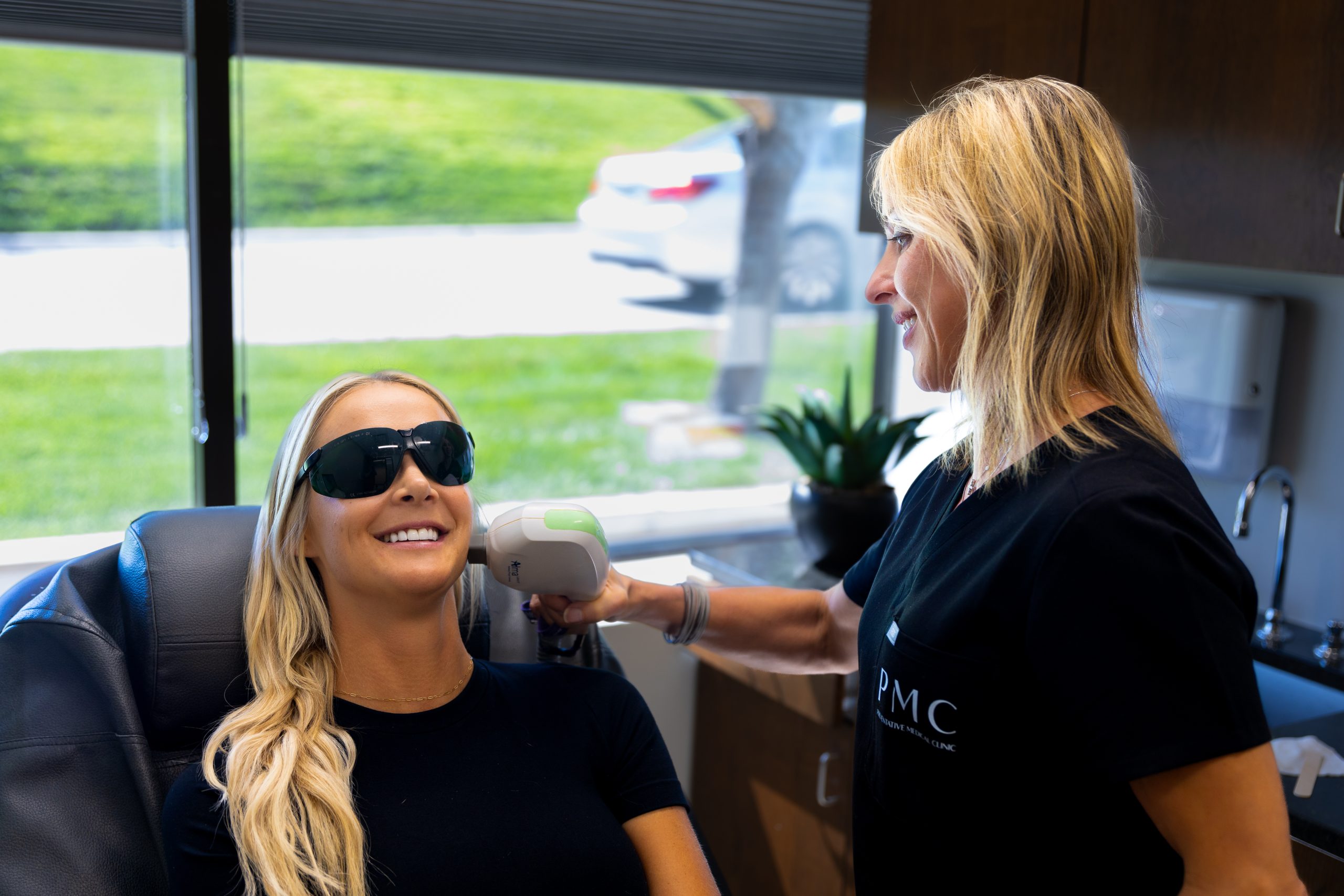 A smiling woman receiving Opus Plasma treatment on her face from a healthcare professional in a clinical setting, enhancing her skin texture and appearance.