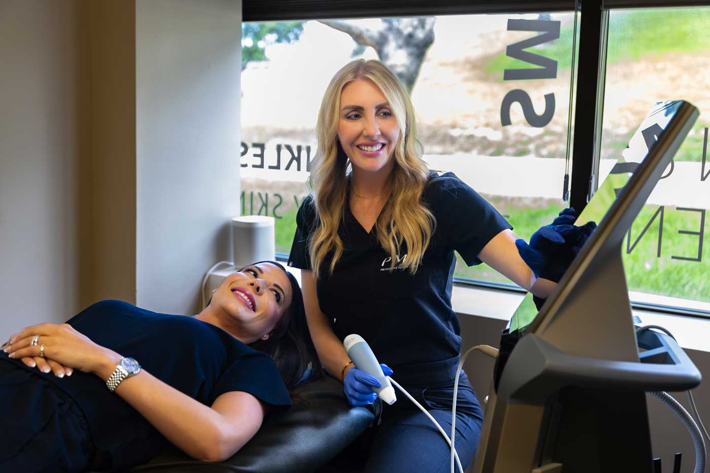 A cheerful patient reclines while receiving a laser skin rejuvenation and skin tightening treatment from a smiling clinician, who operates a sophisticated device in a well-lit medical office.