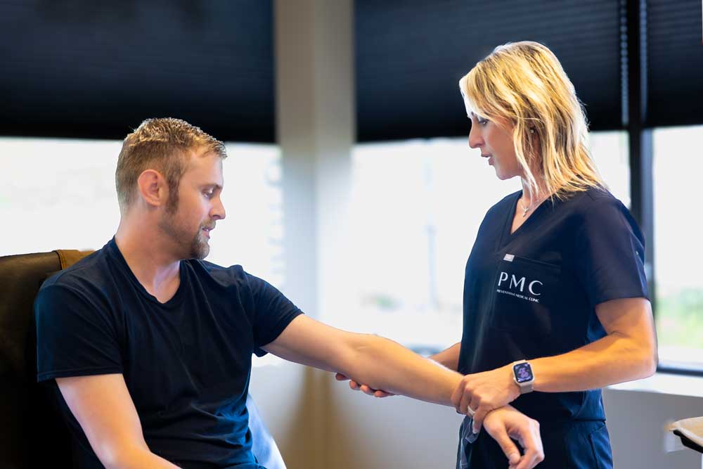 A male patient discusses his tattoo removal treatment with a clinician, who examines his arm in preparation for the procedure in a modern clinic setting.