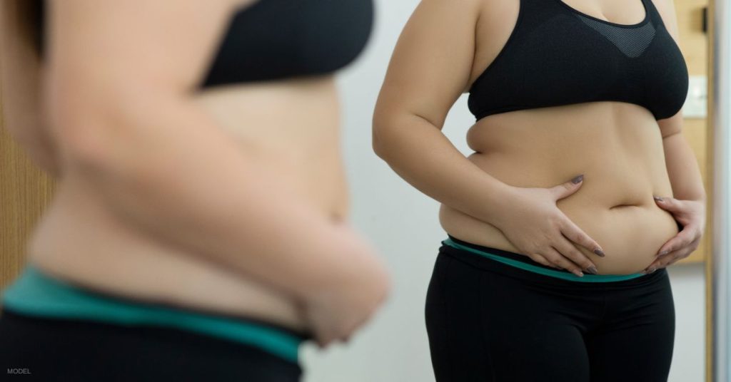 woman standing in front of mirror holding her stomach (model)