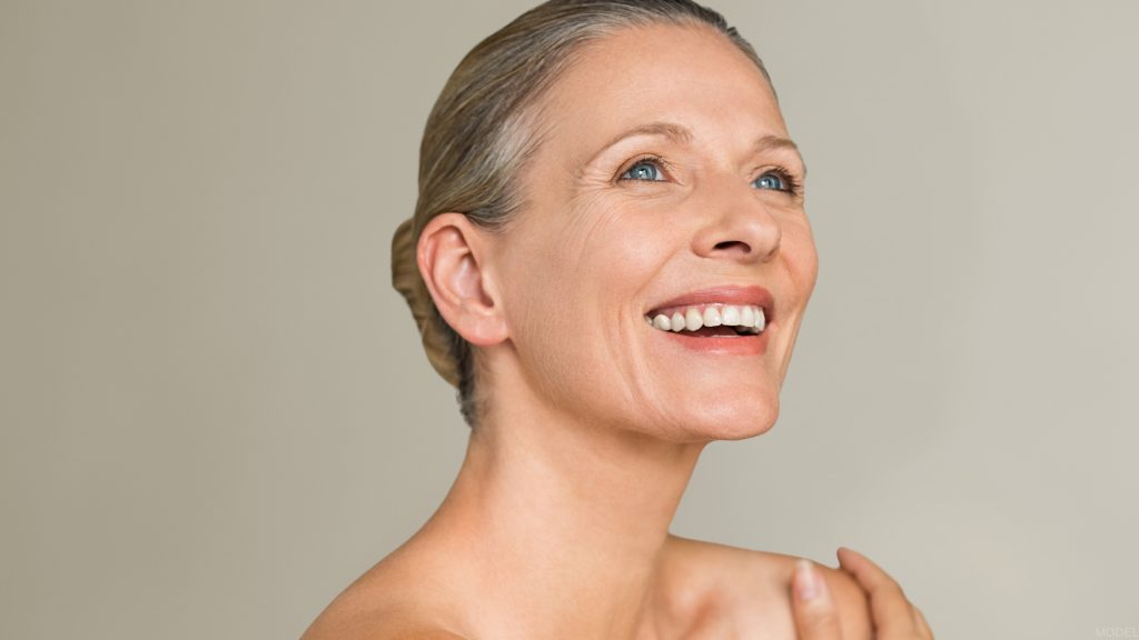 Smiling mature woman posed against a neutral brown backdrop (model)